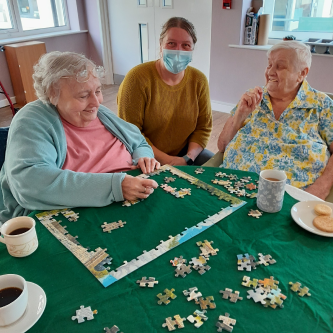 A photo of two residents and one of our staff members sat a table doing a puzzle together