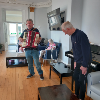 Two men stood in the lounge at Colbury House playing instruments as they entertain our residents