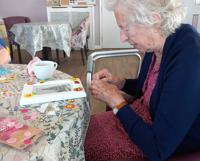 A photo of one of our residents sat at a table decorating a picture frame with stickers and buttons