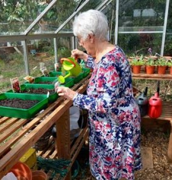 Resident of Colbury House is in the greenhouse watering her seed tray