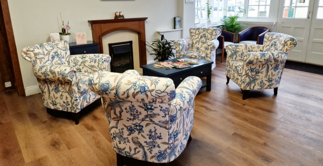 A photo of our reception area at Colbury, with four white and blue floral armchairs situated around a table by our electric fireplace